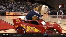 a bulldog is riding a toy lightning mcqueen car on a basketball court