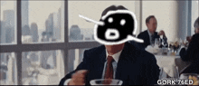 a man in a suit and tie is sitting at a table with gork 76ed on the bottom right