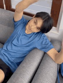 a young man in a blue shirt is laying on a couch with his arms outstretched .
