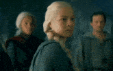 a girl with blonde hair is standing in front of a man and a woman
