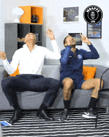 two men sitting on a couch with a sign that says mbappe live on it