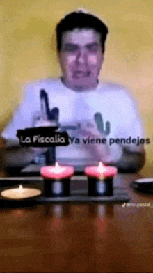 a man is sitting at a table with three candles and a sign that says la fiscalia ya viene pendejos .