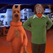 scooby doo is standing next to a man in a green sweater .