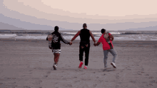three people holding hands on a beach with one wearing a shirt that says ' coca cola '