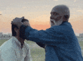 a man with a beard is touching another man 's head in a field