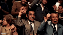 a group of people are sitting in a stadium with their hands in the air and the word ballan is on the bottom right