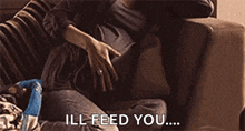 a pregnant woman is sitting on a couch with her hands on her belly and the words ill feed you