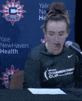 a man is laughing in front of a microphone in front of a wall that says yale newhaven health