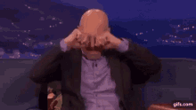 a bald man is sitting on a couch with his hands on his face .
