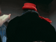 a man wearing a red hat and a black coat is standing next to a window .