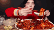 a woman in a red shirt is eating a plate of food with chopsticks