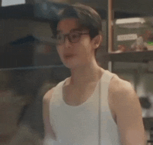 a young man wearing glasses and a white tank top is standing in front of a window .