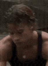 a young man wearing a black tank top and a necklace is looking at the camera .