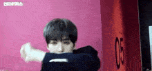 a young man is standing in front of a pink wall making a funny face .