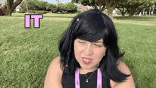 a woman in a black top is sitting in the grass with the word it above her head
