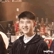 a young man is smiling in front of a bar with bottles of alcohol .