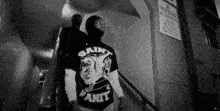 a man in a saint vanit t-shirt is walking down stairs .