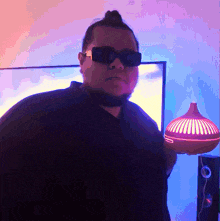 a man wearing sunglasses and a black shirt holds a red lamp