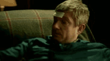 a man is laying on a couch with a sticker on his forehead that says ' a ' on it .
