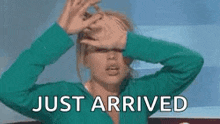 a woman in a green sweater is covering her face with her hands and the words `` just arrived '' behind her .