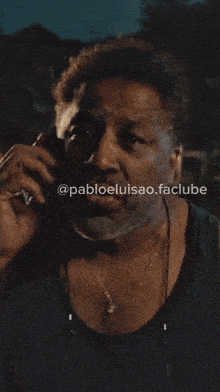 a man wearing a black tank top is talking on a cell phone with a purple sticker that says uma desgraça