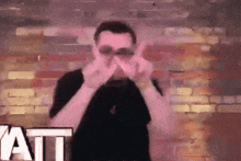 a man wearing sunglasses is giving the middle finger in front of a brick wall and the word att