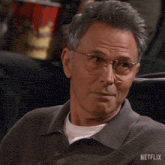 a man wearing glasses is sitting in front of a bucket of popcorn that says netflix on it