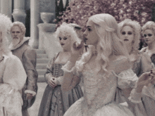 a woman in a white dress stands in front of a group of women