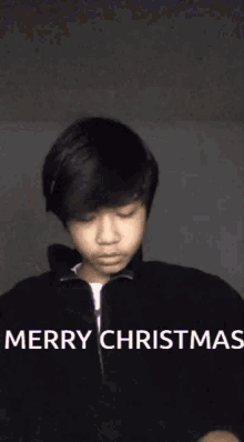 a young boy is wearing a black jacket and says merry christmas .