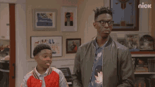 a man and a boy are standing next to each other in a room with a nick logo on the corner