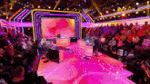 a large group of people are sitting in front of a stage with a pink background