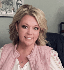 a woman wearing a pink vest and a white shirt smiles