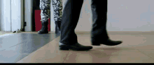 a man in a suit and black shoes is walking on a tile floor