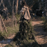a woman in a dress made of grass and flowers stands in the woods