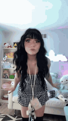 a girl in a plaid dress is standing in a room with stuffed animals on the shelves .