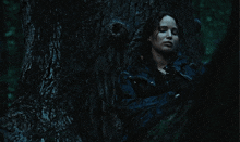 a woman leans against a tree in the dark with her eyes closed