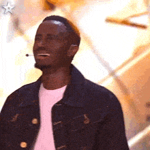 a man wearing a denim jacket and a white shirt is laughing with a microphone in his ear