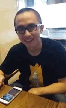 a man wearing glasses sits at a table with a cell phone in front of him