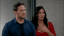 a man and a woman are standing next to each other in front of a window in a room .