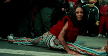 a woman in a red shirt and striped pants is doing a split on the street
