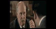 a man in a suit and tie is talking to another man in a room .
