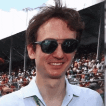 a man wearing sunglasses is smiling in front of a crowd of people