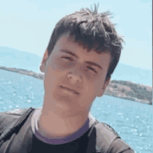 a young man is posing for a picture in front of the ocean .