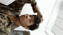 a man in a camo shirt holds his hand to his forehead