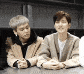 two young men are sitting next to each other with their hands folded