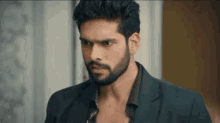 a man with a beard is wearing a suit and a black shirt and looking at the camera .
