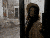 a woman wearing a hat is standing in front of a window with a bicycle in the background