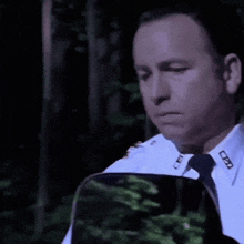 a police officer in a white shirt and tie is looking down at something .