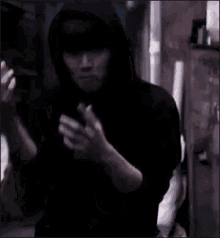 a man in a black hoodie is standing in a dark room with his hands in his pockets .