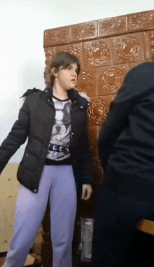 a girl in a black jacket and purple pants stands in front of a man in a black jacket